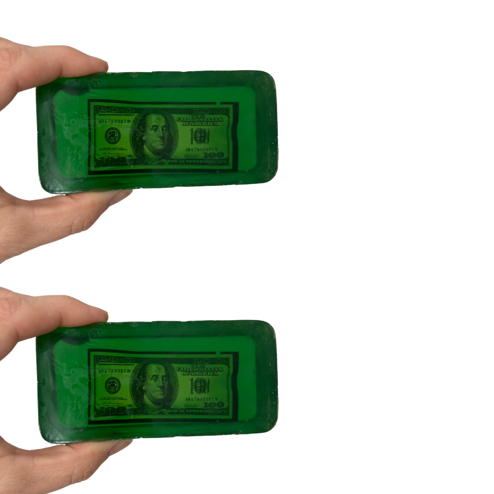Two green bars of soap with dollar bill design held by a hand on a white background
